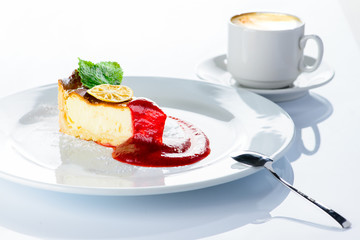Delicious cheesecake with jam, citrus, mint and powdered sugar on the plate and a cup of cappuccino on white background