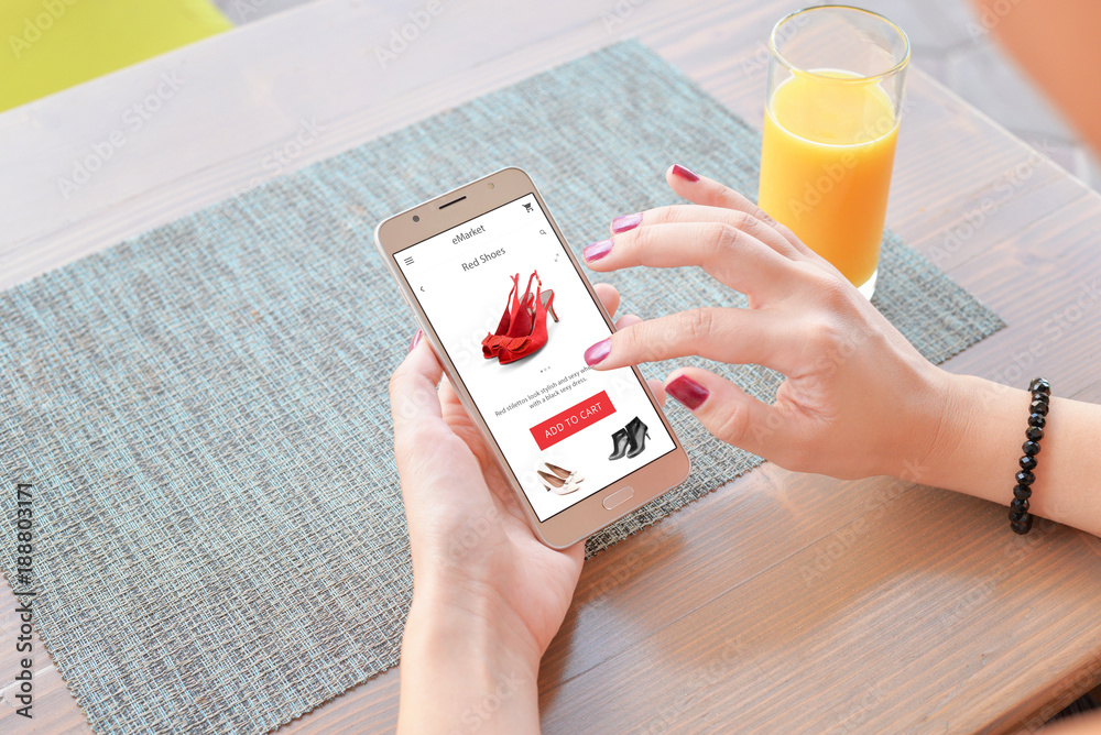 Poster woman buy red shoes online . mobile app or web site on screen. table and juice in background.