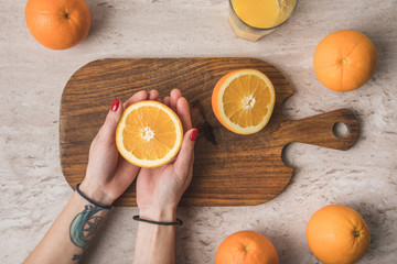 cropped image of woman holding orange half in hands