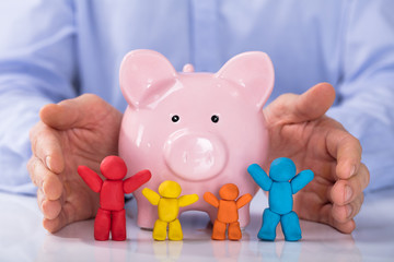 Hand Protecting The Piggybank With Colorful Family