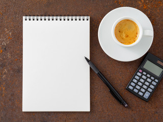 clean white sheet in an open spiral-bound pad, pen, calculator and Cup of coffee on the iron of the rusty metal table, top view