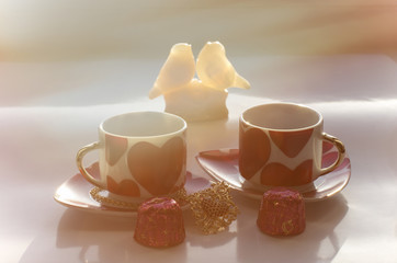 Beautiful sunny morning on Valentine's day with festive symbols on mugs and gift in heart shape for women and figurines of doves