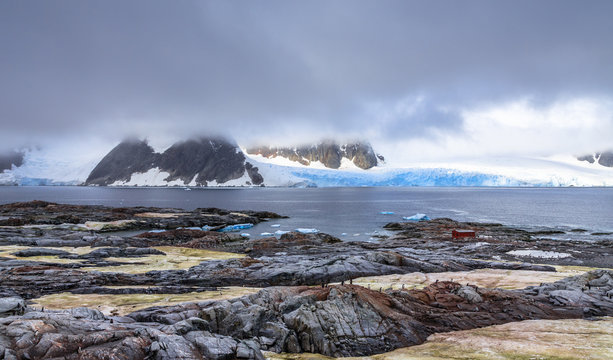 Rocky coastline panorama with mountains and blue glaciers hidden in clouds, Peterman island, Antarctic peninsula