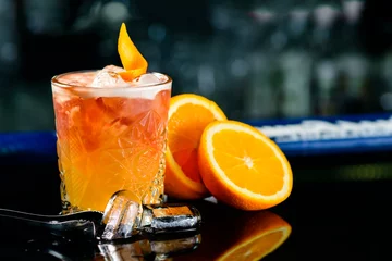 Poster Closeup glas klassieke alcohol cocktail peetvader op de bar met schijfje sinaasappel en ijsblokjes © smspsy