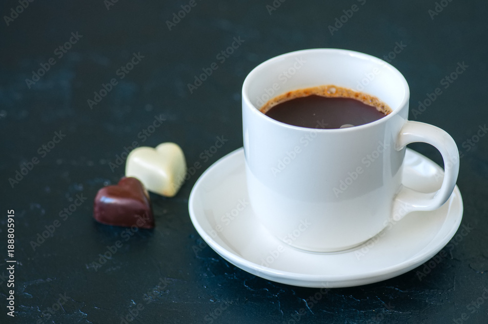 Wall mural cup of strong coffee and heart shaped dark and white chocolates on a black background.