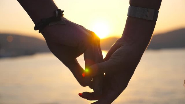 Male and female hands comforting and stroking each other at sunset against an sea background. Young couple joining arms outdoor. Summer vacation. Concept of loving and happiness. Close up Slow motion