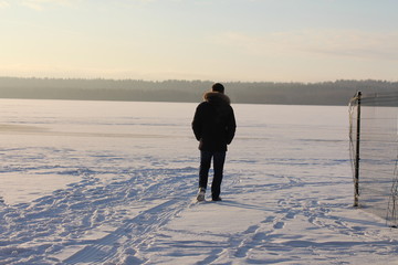 A man walking on the ice lake. A view from the back.

