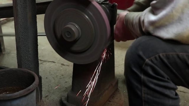 Man sharpening axe at a whetstone in a grindery