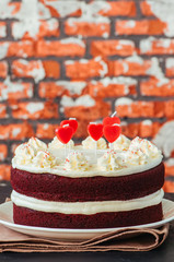 Red velvet cake with cream cheese frosting and heart shaped red candles on a white plate