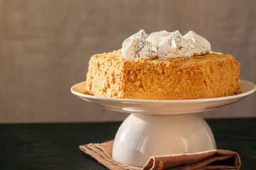 Honey cake with meringue decoration on top served on a white plate on a black backdrop.