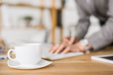selective focus of cup of coffee on table with businesswoman making notes
