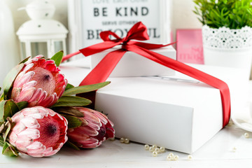 Selective focus on red flowers, on the background white present box with red ribbon. Concept of surprise, anniversary, Christmas, Birthday, New Year and Valentines Day