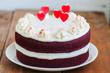 Red velvet cake with cream cheese frosting and heart shaped red candles on a white plate