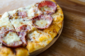 Cut into slice serving pizza with pepperoni sausage on a wooden board on the table.