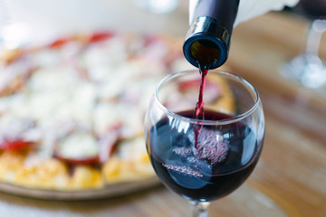 Czerwone wino wlewa się z butelki do kieliszka w restauracji lub kawiarni, w tle widać sylwetkę pizzy. - 188810749