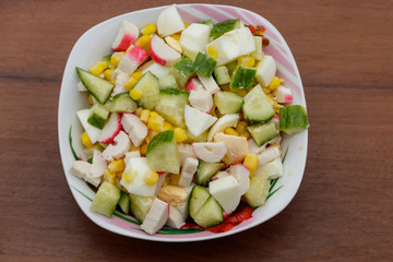 Salad with crab sticks, sweet corn, cucumber and eggs on wooden table