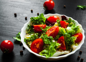 various fresh mix salad leaves with tomato in bowl on dark wooden background
