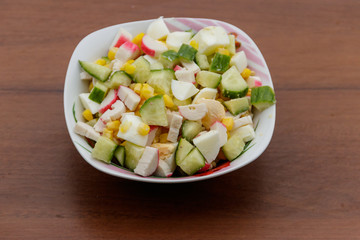 Salad with crab sticks, sweet corn, cucumber and eggs on wooden table