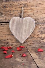 big wooden heart on a plank  with red petals of roses on a plank