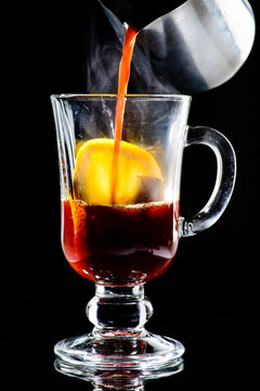 Process of preparing hot non-alcoholic mulled wine with orange and cinnamon on dark background