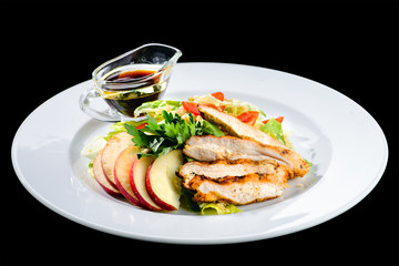 Roasted juicy pork steak with apples and soy sauce in a white plate isolated on black background