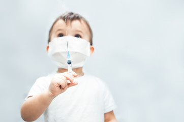 The child in the mask of the doctor with syringe in hands sprinkles, pours on a gray background