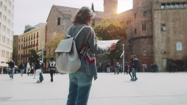Rear view of young tourist woman looking at tourist map and exploring sightseeing of Barcelona, hipster girl walking in Barcelona city streets,slow motion, enjoying holiday concept, lifestyle