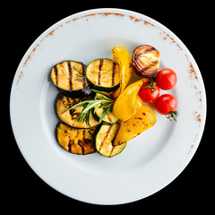 Tasty baked eggplant with spices and tomato in a white plate on dark background. Top view, flat lay