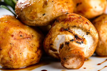 Delicious appetizing baked mushrooms with sauce in a white plate on dark background. Food background
