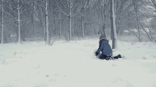 Small boy builds snowman. Family plays in snow. Yougster enjoys winter fun. Winter landscape with child and falling snow. Everything is covered with fresh powder. Winter background, Christmas theme.
