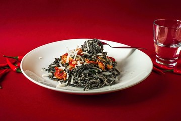 Black spaghetti with roasted tomato, hot chilli peppers, ricotta and parmesan cheese on white plate