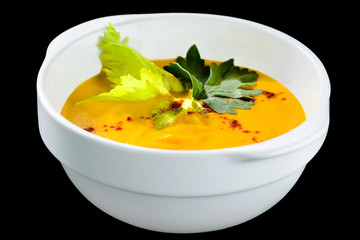 Healthy tasty carrot cream soup with parsley in a white plate isolated on black background