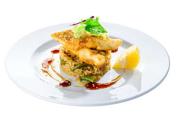 Delicious fried cod fillet with risotto, salad and lemon in a white plate isolated on white background