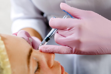 Close-up of a beautician injects Botox injection into the cheekbones of a young woman to correct the form in the medical office