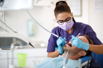 Young female dentist drilling tooth to patient