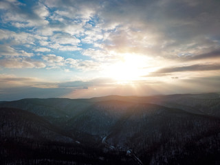 Aerial view of snowy forest with road during sunset time