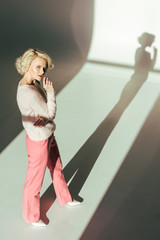 high angle view of beautiful blonde woman in trendy pink clothes looking at camera in studio