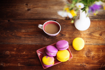 A cup of hot black coffee and bright macaroons on a wooden table at dark background with colorful bokeh