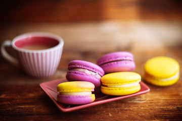 A cup of hot black coffee and bright macaroons on a wooden table at dark background with colorful bokeh