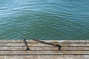 Metal chains on wooden pier at sea.