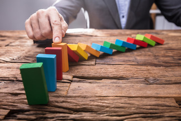 Businessperson Stopping Colorful Falling Dominos With Finger