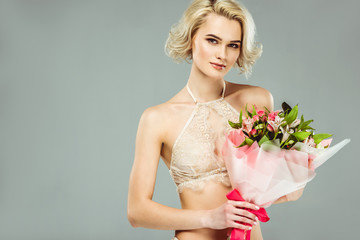 attractive blonde girl in lace bra with bouquet of flowers, isolated on grey