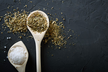  Wooden spoon with Italian seasoning - dried oregano with thyme, basil and vegetables .Oregano in a wooden spoon on a rocky concrete dark black background with a place for text Top view. A wooden spoo