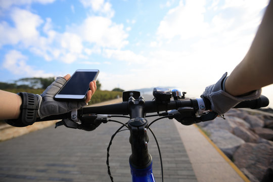 Cyclist using smartphone for navigation when riding mountain bike on the coast path