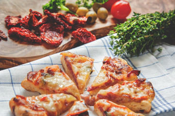 Pieces of Margarita pizza on a napkin with sun-dried tomatoes and olives with a large bundle of the herb thyme . Selective focus.