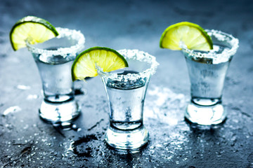 Tequila shot with lime slices and salt on dark background