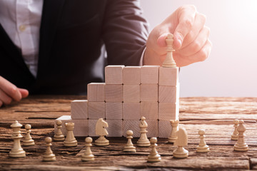 Businessperson Arranging Chess Piece On Wooden Blocks