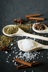  Wooden spoon with Italian seasoning-dried oregano with thyme, basil and vegetables.Oregano in a wooden spoon on a rocky concrete dark black background with a place for text.Top view.salt crystals pep