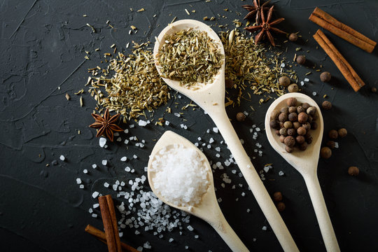  Wooden spoon with Italian seasoning-dried oregano with thyme, basil and vegetables.Oregano in a wooden spoon on a rocky concrete dark black background with a place for text.Top view.salt crystals pep