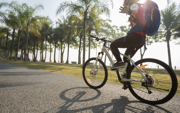 woman cyclist riding bike with outstretched arms in tropical park